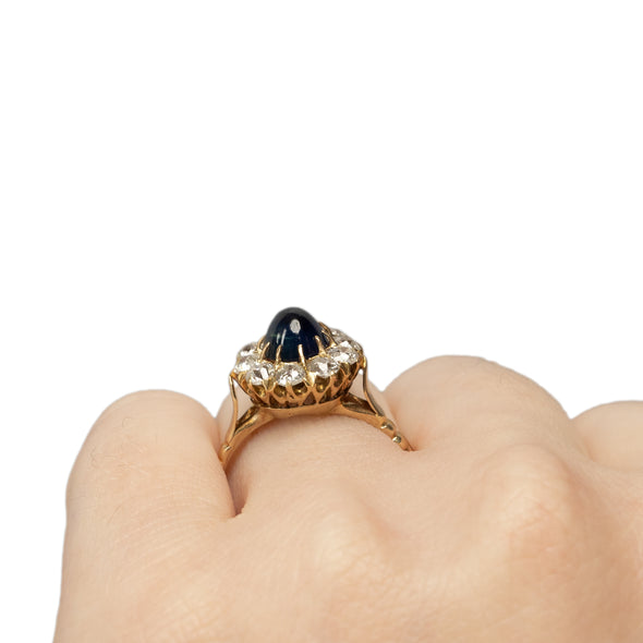 Victorian 14K Yellow Gold Deep Blue Cambodian Cabochon Sapphire and Old European Cut Diamond Halo Cocktail Ring on the hand from the back showing off the height 