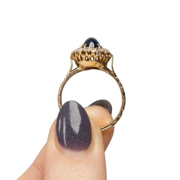 Victorian 14K Yellow Gold Deep Blue Cambodian Cabochon Sapphire and Old European Cut Diamond Halo Cocktail Ring in the hand showing the overall profile 