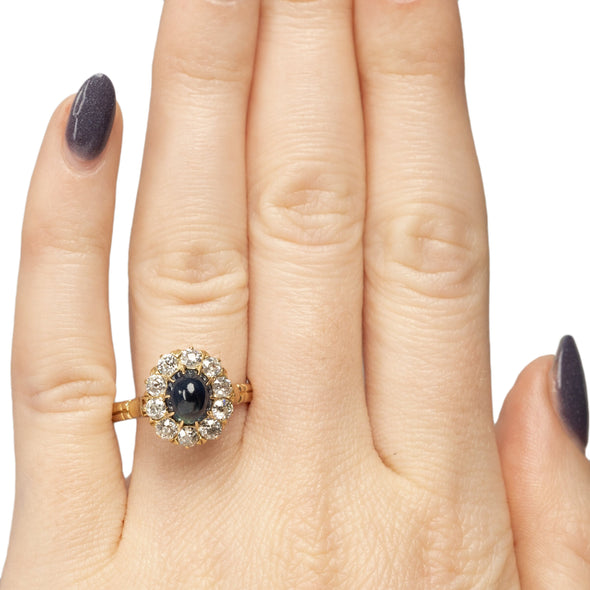 Victorian 14K Yellow Gold Deep Blue Cambodian Cabochon Sapphire and Old European Cut Diamond Halo Cocktail Ring on the hand form the top highlighting the overall look 