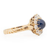 Victorian 14K Yellow Gold Deep Blue Cambodian Cabochon Sapphire and Old European Cut Diamond Halo Cocktail Ring from the left showcasing the cathedral shanks and prong settings 